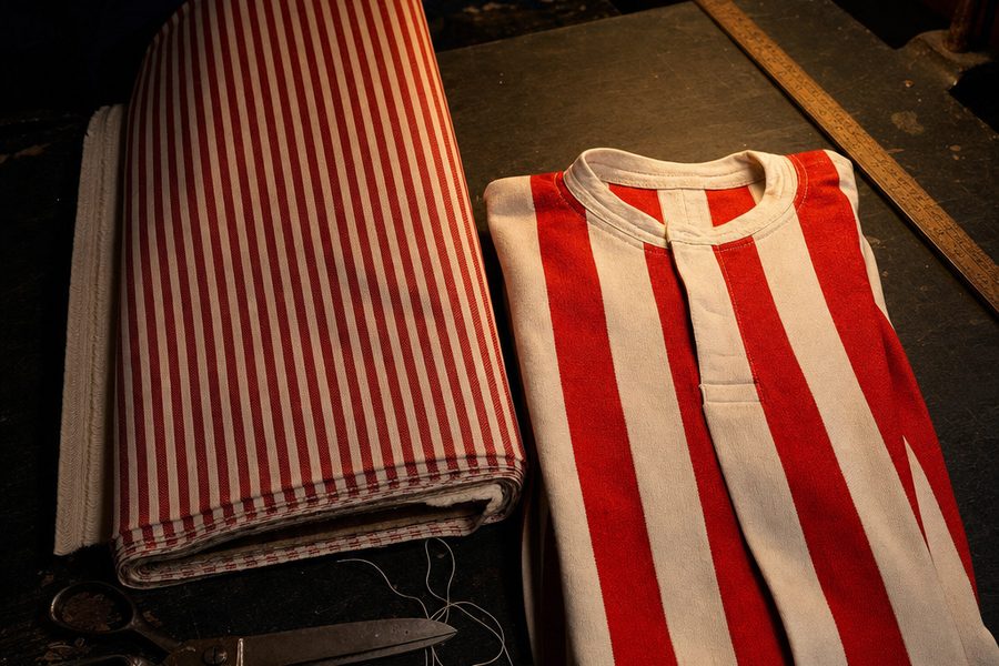 A bolt of red-and-white striped mattress ticking beside a plain striped football jersey on a workshop table