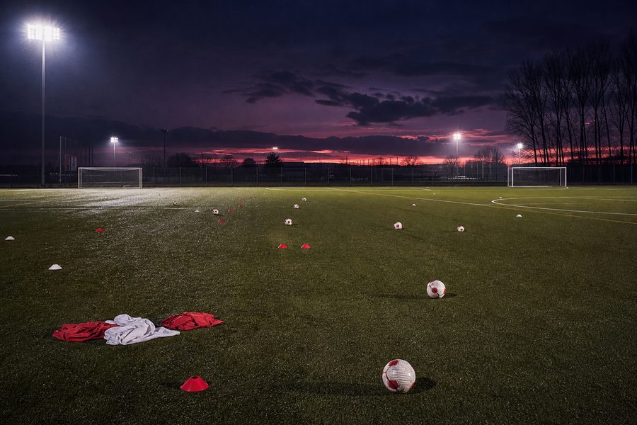 Empty floodlit training pitch at dusk scattered with balls and low cones
