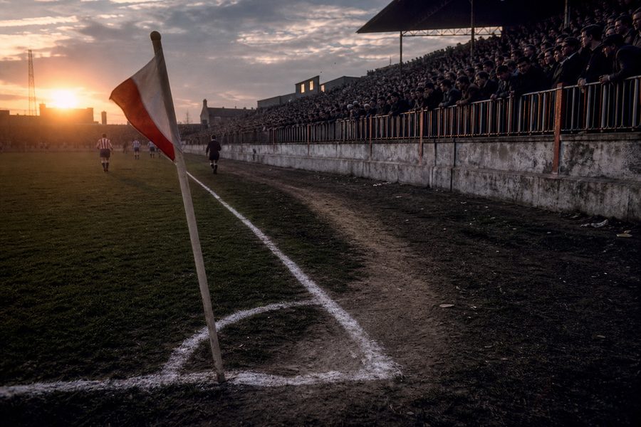 Grass worn bare along a touchline running to a red and white corner flag