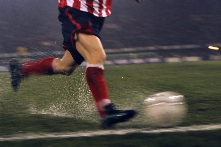 Motion-blurred legs of a winger cutting inside at speed along a floodlit flank