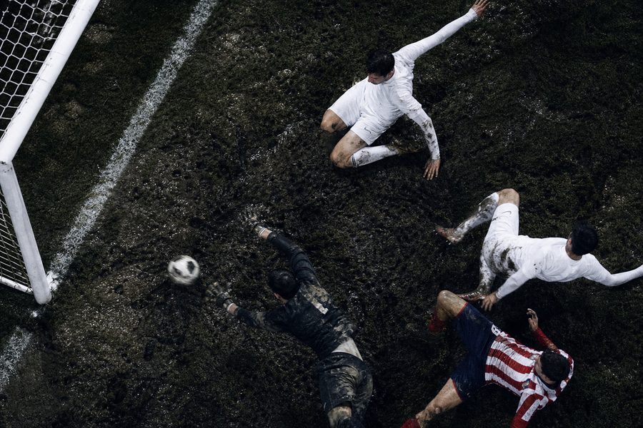 Overhead view of a muddy goalmouth, the ball past a diving goalkeeper and players sprawled on the turf