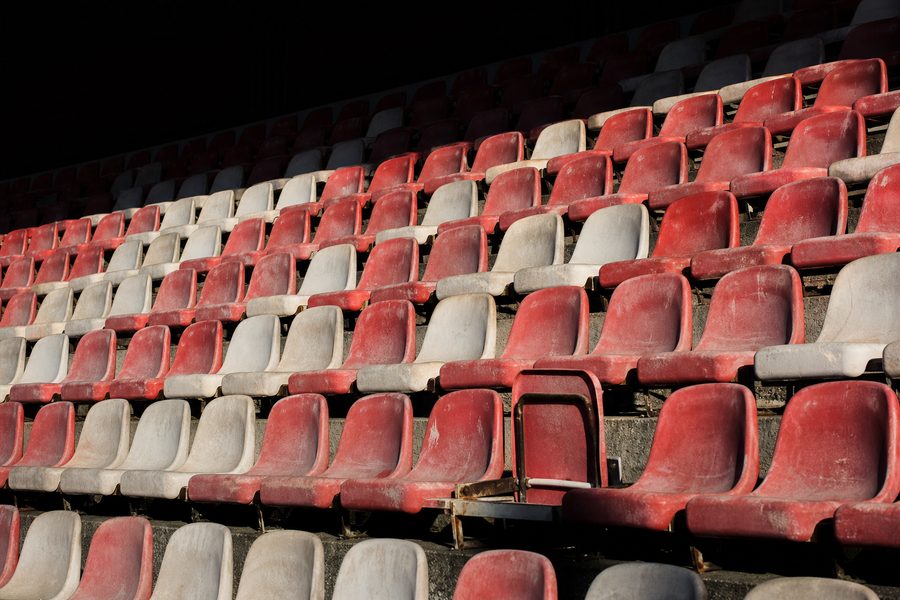Rows of empty sun-faded red and white bucket seats in an old stand
