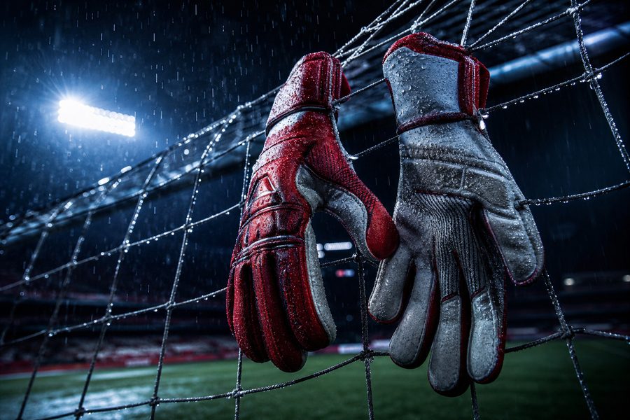 Goalkeeper gloves hooked over a goal net in the rain, water beading on the leather