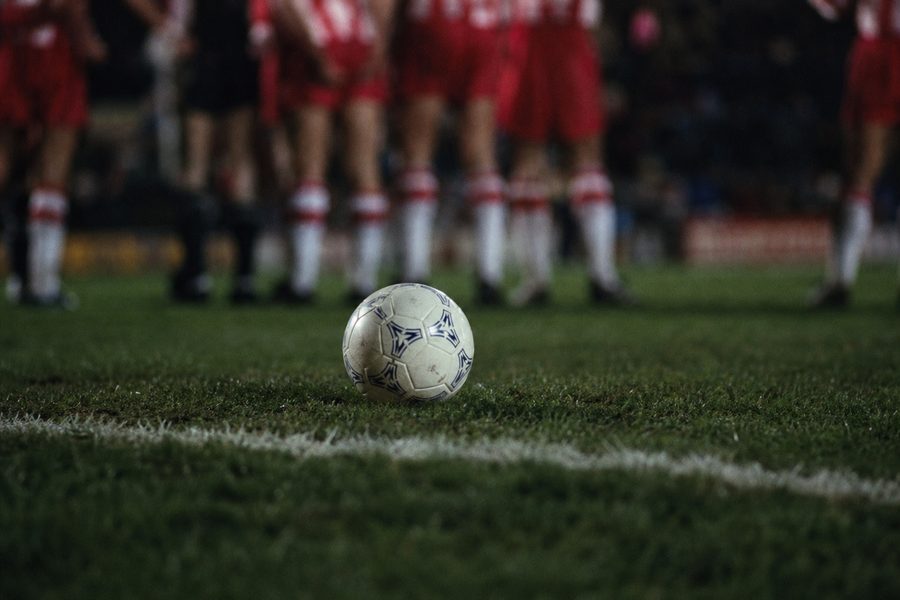 Ball standing still on the grass in front of a blurred wall of defenders' legs