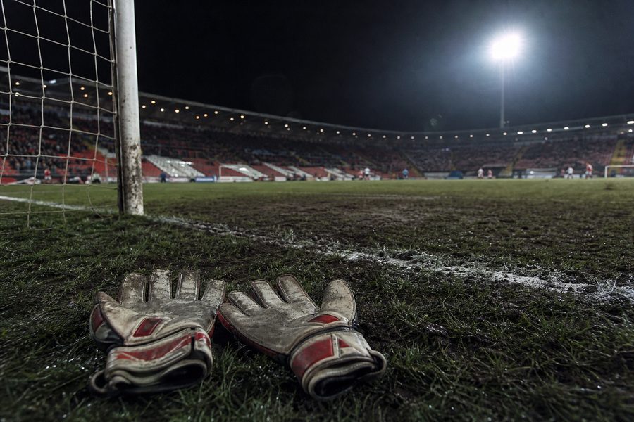 Worn goalkeeper gloves lying on the grass beside a goalpost under floodlights